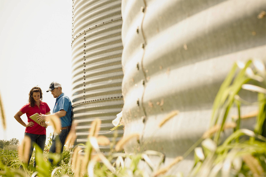 Farmer and retailer strategize a farm plan near grain bins.