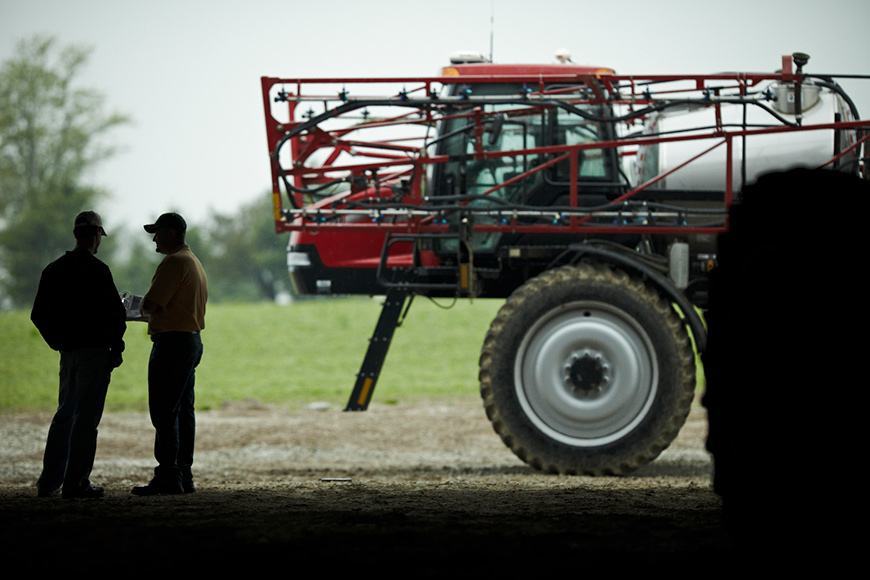Two men assessing weed management plan standing by sprayer
