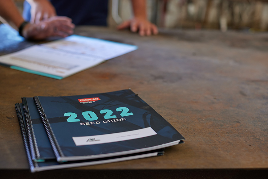 2022 CROPLAN seed guide on a table with farmer and retailer in the background.
