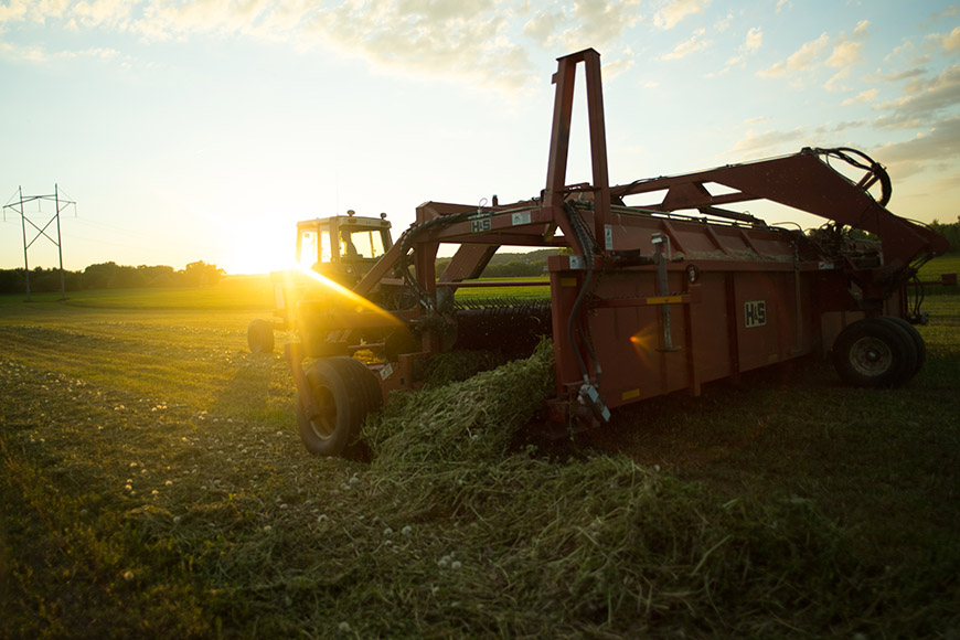 Tractor swathing an alfalfa field at sunset