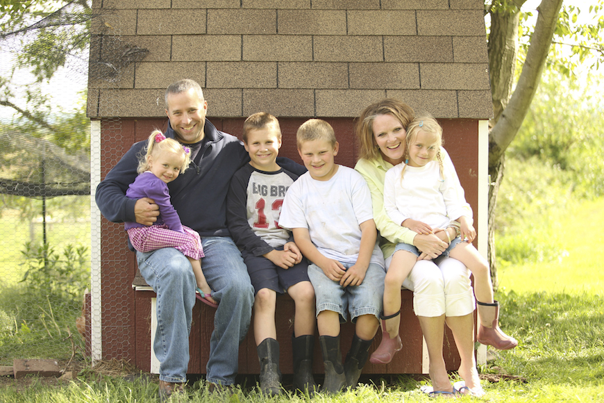 Family photo of mom, dad and four kids on bench in front of red barn