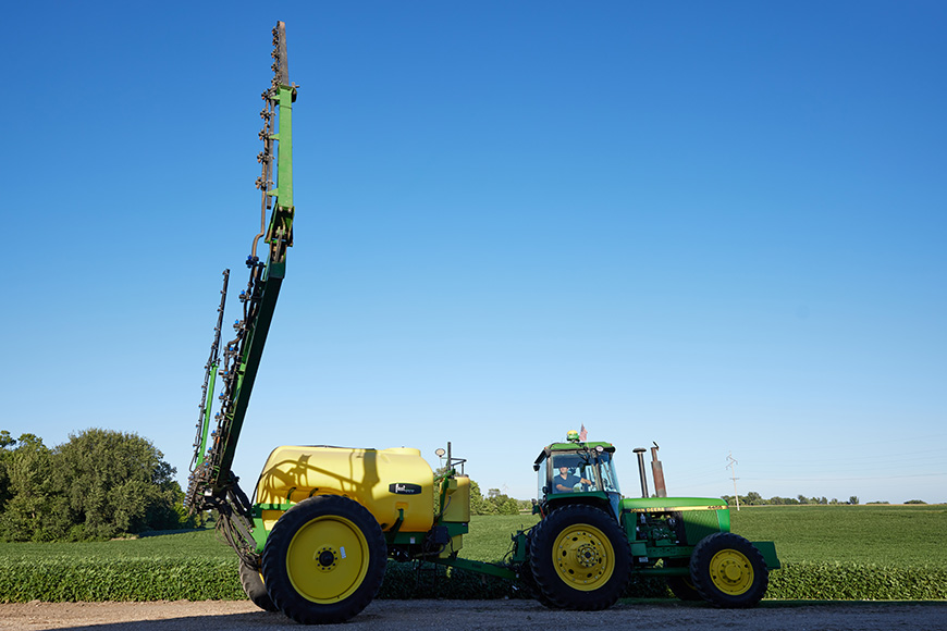 Farmer lowering a spray boom to prepare for an herbicide application.