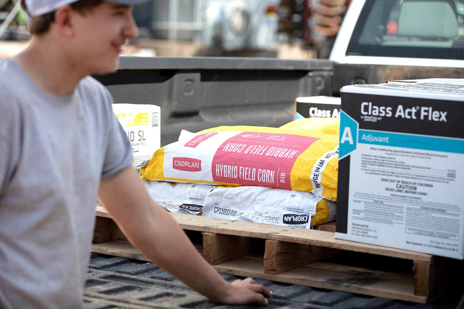 Farmer and retailer talking near a truck tailgate full of seed.